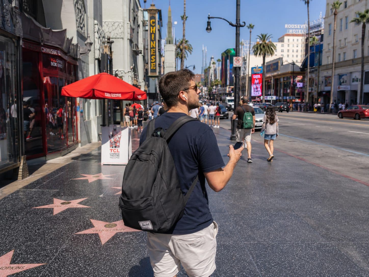 A traveler exploring Hollywood Boulevard with a phone and wireless earbuds.